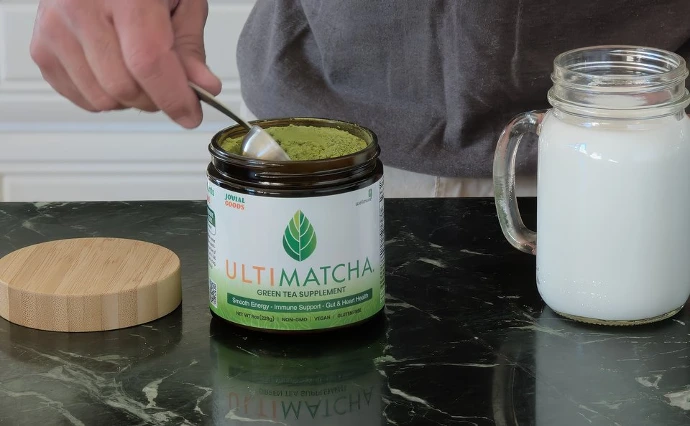 A man scooping Ultimatcha powder into a shaker filled with milk 