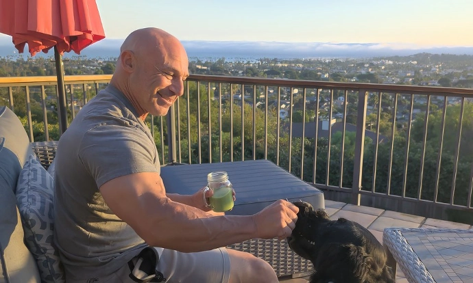 Middle aged male with big muscles drinking Ultimatcha while playing with a dog with a nice view in the background